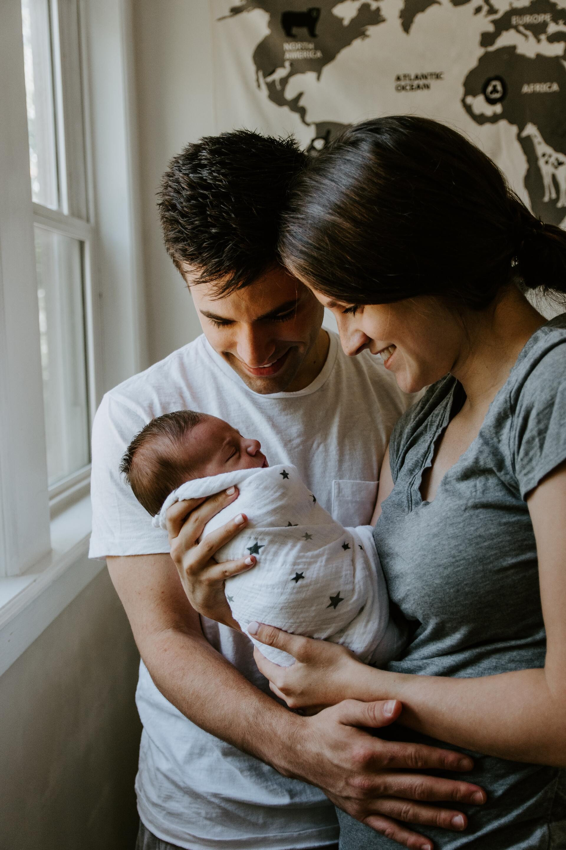 Parents holding a sleeping newborn wrapped in a white blanket indoors