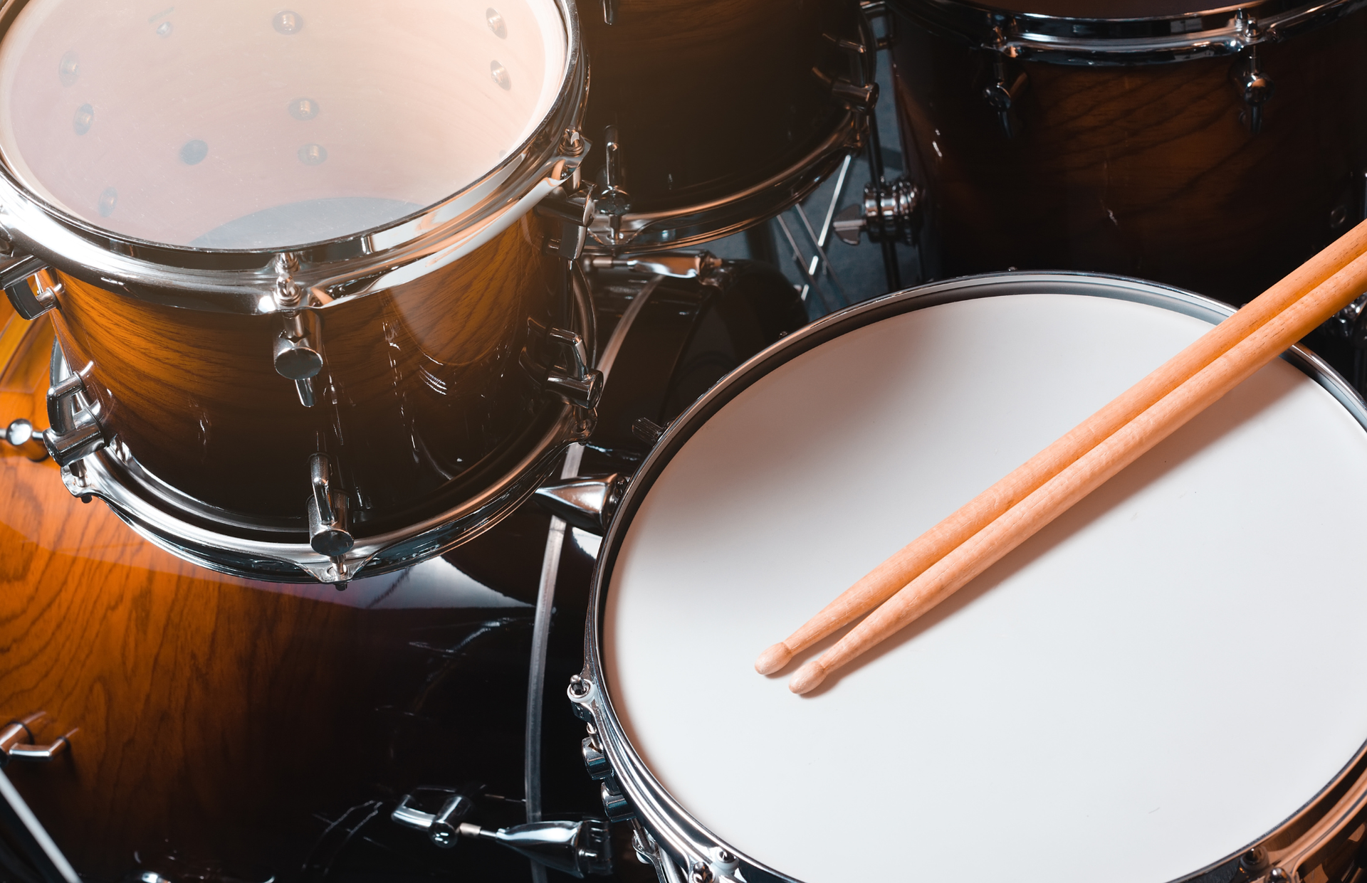 Close-up of a drum kit with white drumheads, black shells, and orange drumsticks resting on a snare drum.