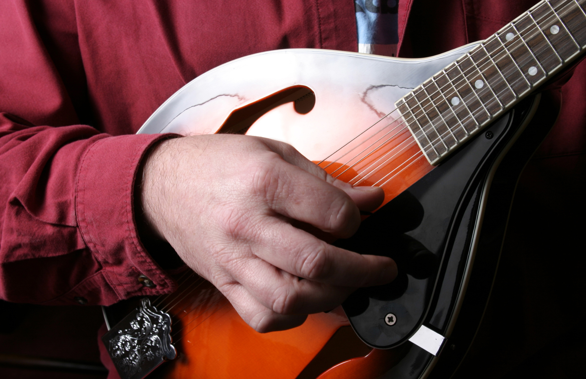 Close-up of a hand playing an orange mandolin against a red shirt