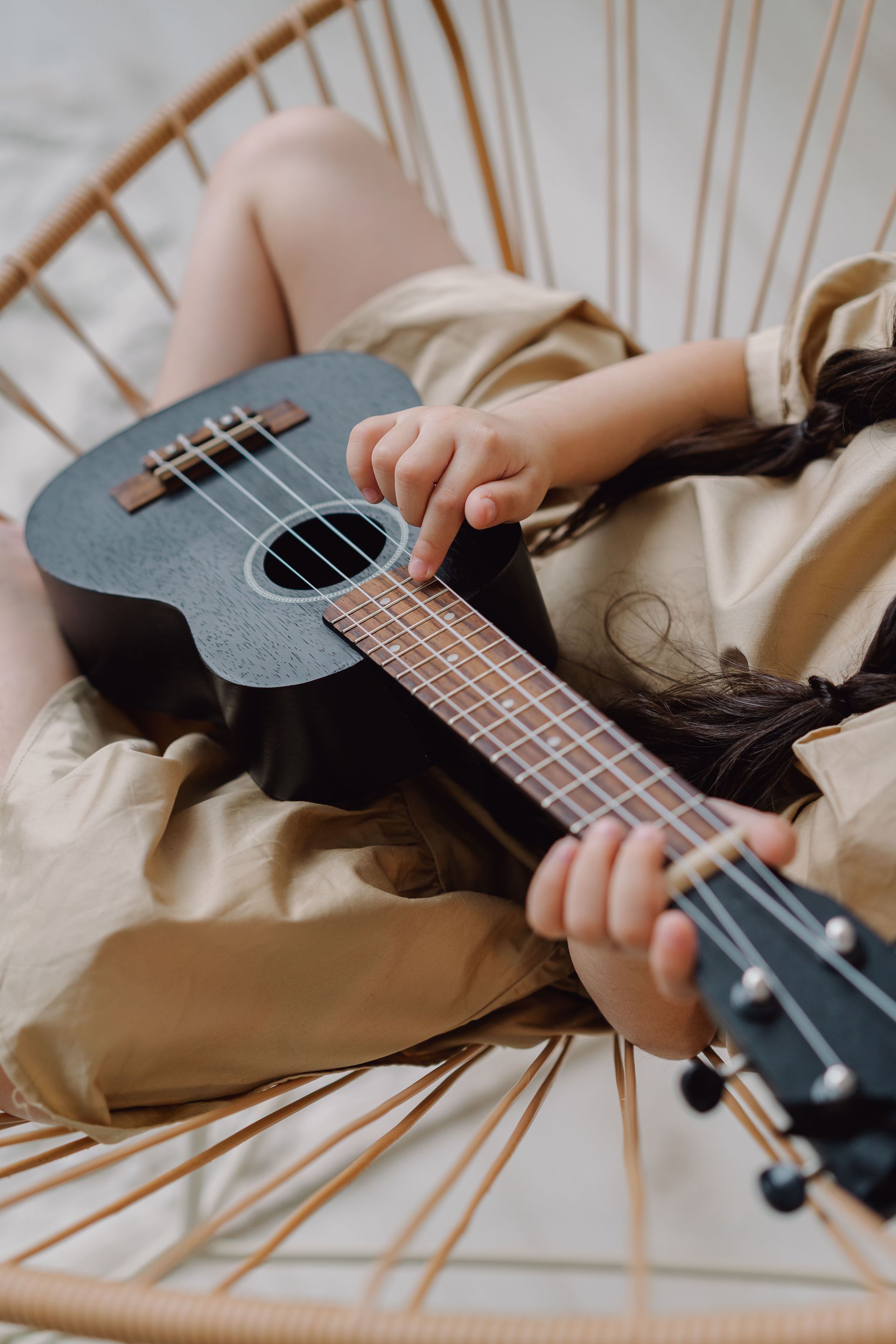 Person playing a small guitar-like instrument indoors near a bright window