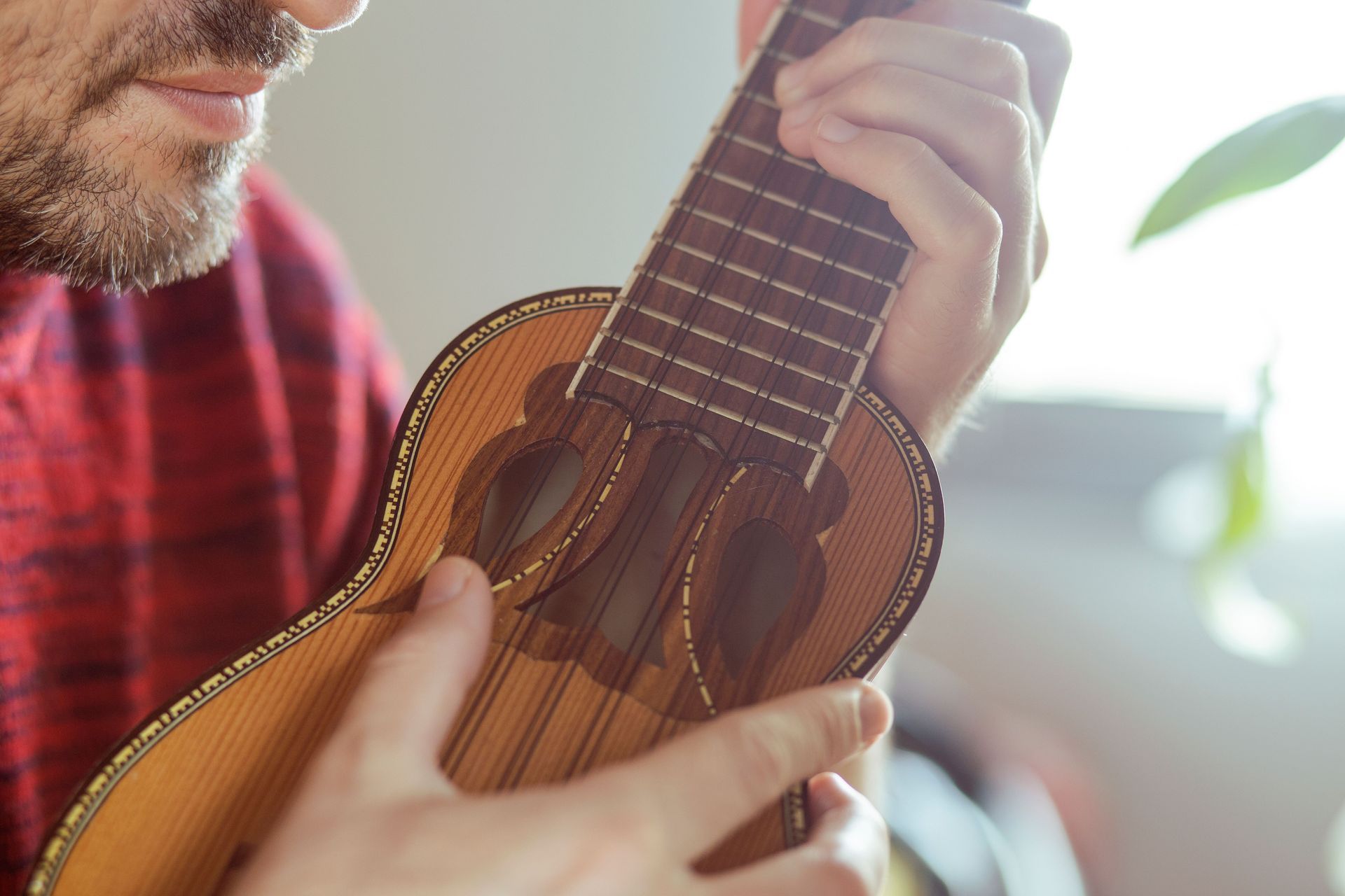 Hands playing a brown ukulele outdoors, close-up on the strings and body.