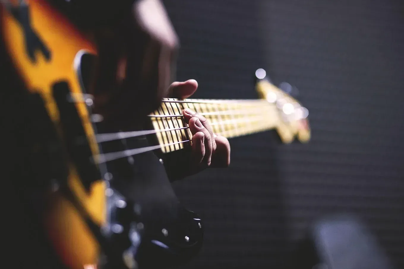 Close-up of a hand playing a sunburst electric bass guitar in dim lighting