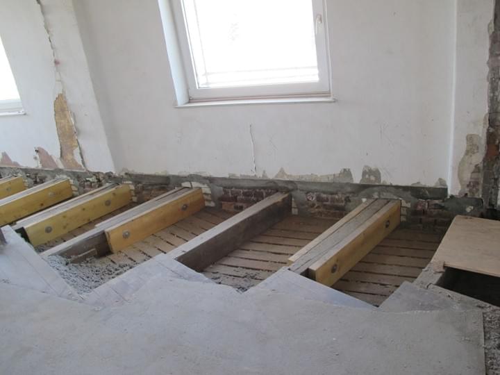 Innenansicht einer Baustelle mit freiliegenden Bodenbalken und Beton, im Hintergrund ein Fenster.