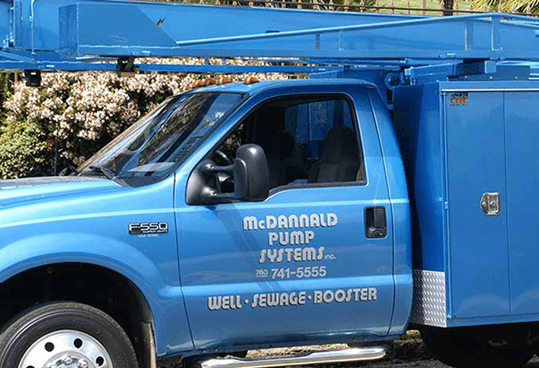 Two workers in reflective vests lift a manhole cover beside a utility truck in a yard.