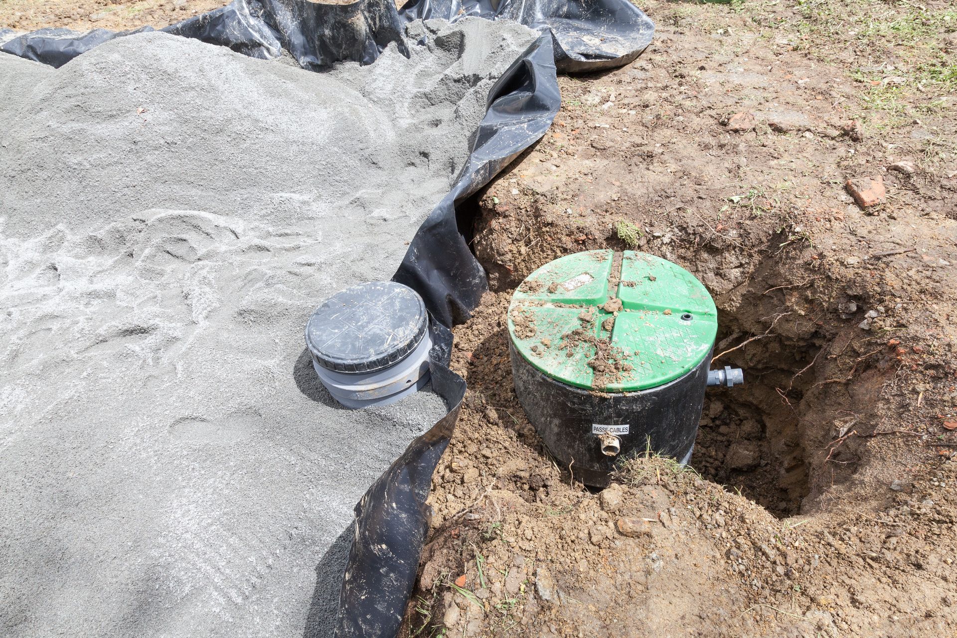Green utility cap beside a black geotextile edge in a dirt excavation area