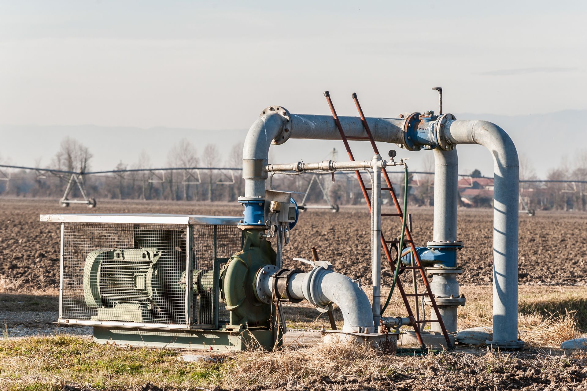 Outdoor industrial gas pipeline with valves and pipes in a dry field, with distant hills in the background