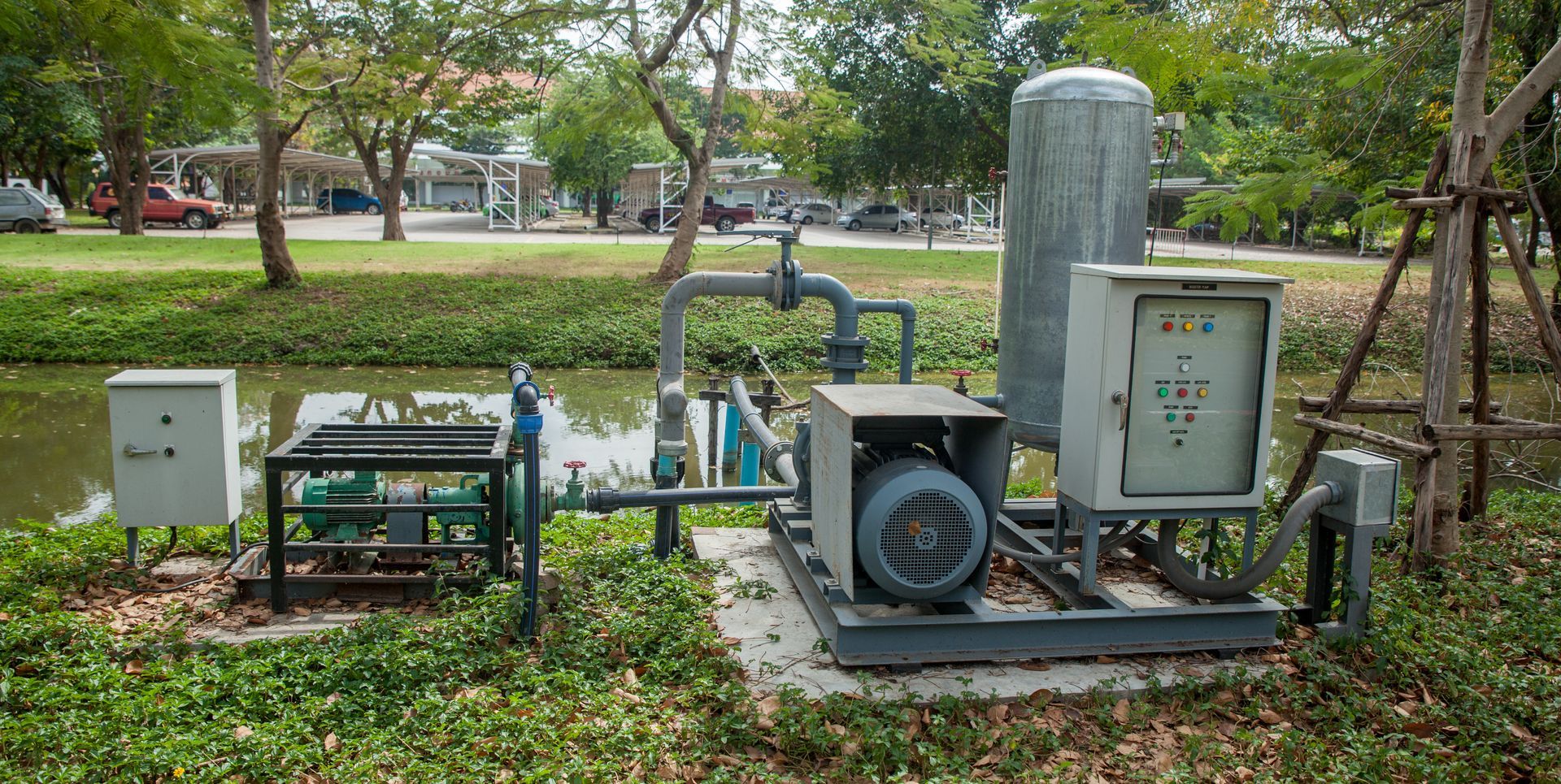 Outdoor utility equipment and control boxes in a grassy park area with trees and walkway behind.