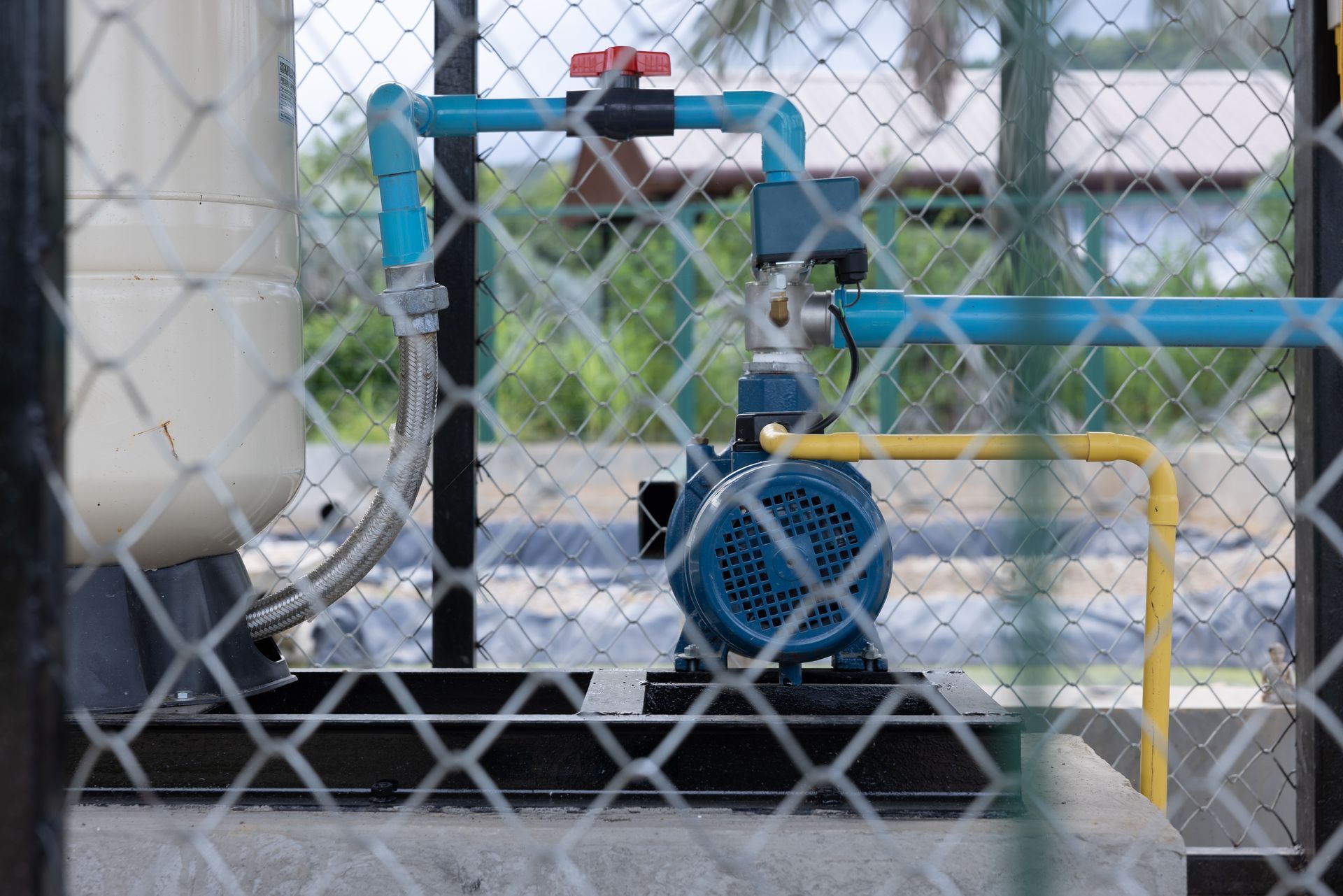 Blue industrial pump and pipes behind a chain-link fence in a utility area
