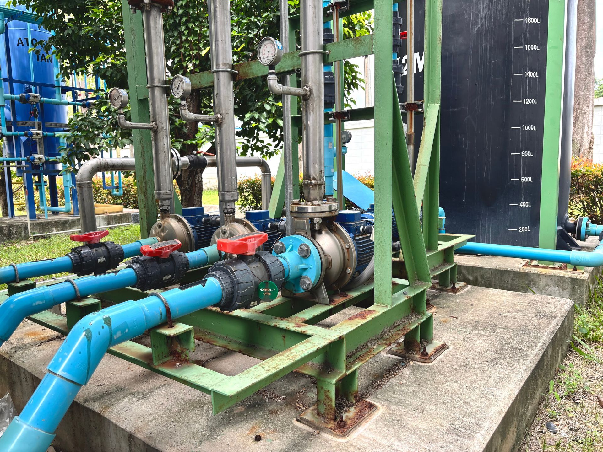 Blue industrial pipes and valves beside a black storage tank in an outdoor facility