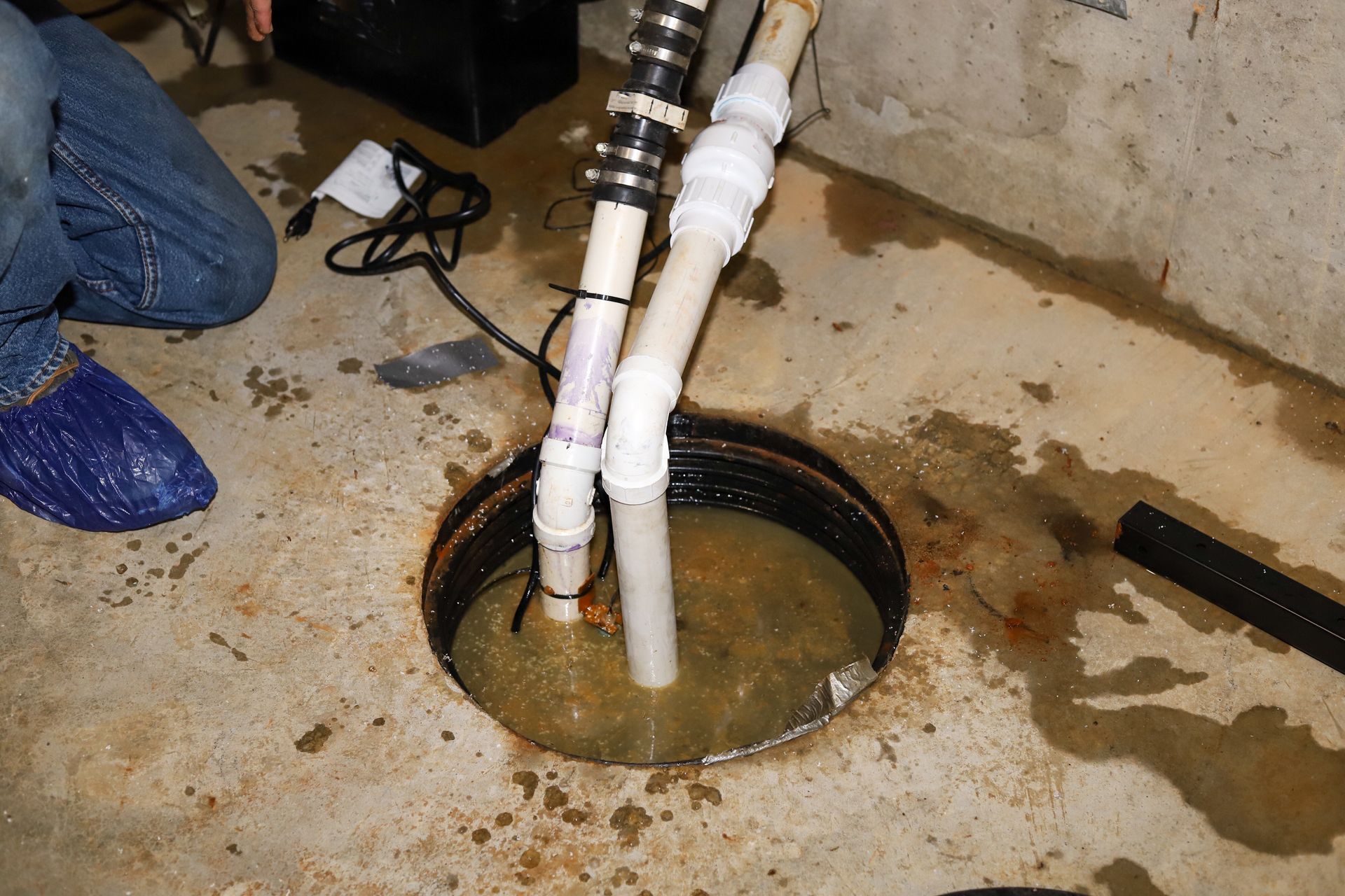 Plumbing pipes entering a flooded floor drain in a concrete basement area