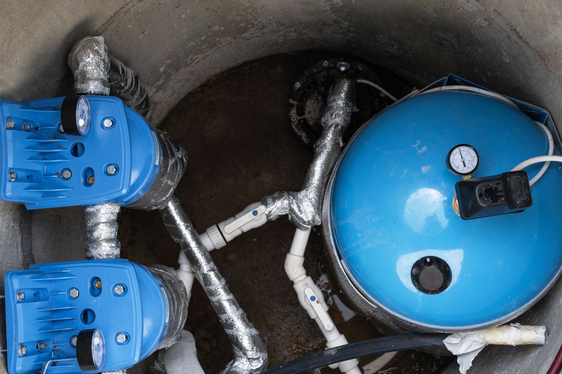 Blue water meter valves and pipes inside a concrete utility chamber