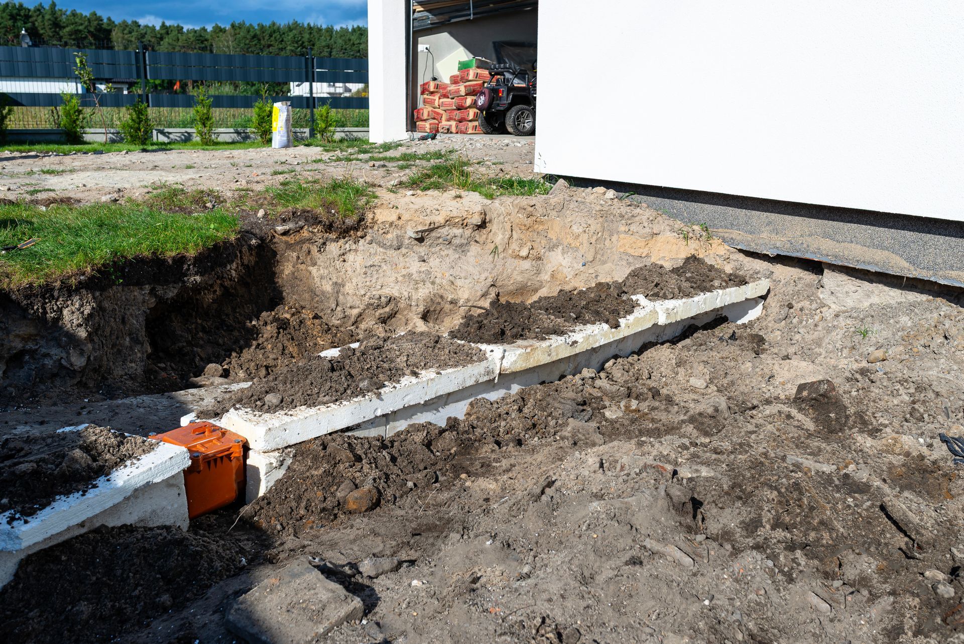 Excavation trench beside a white building with a partially exposed pipe and orange coupler