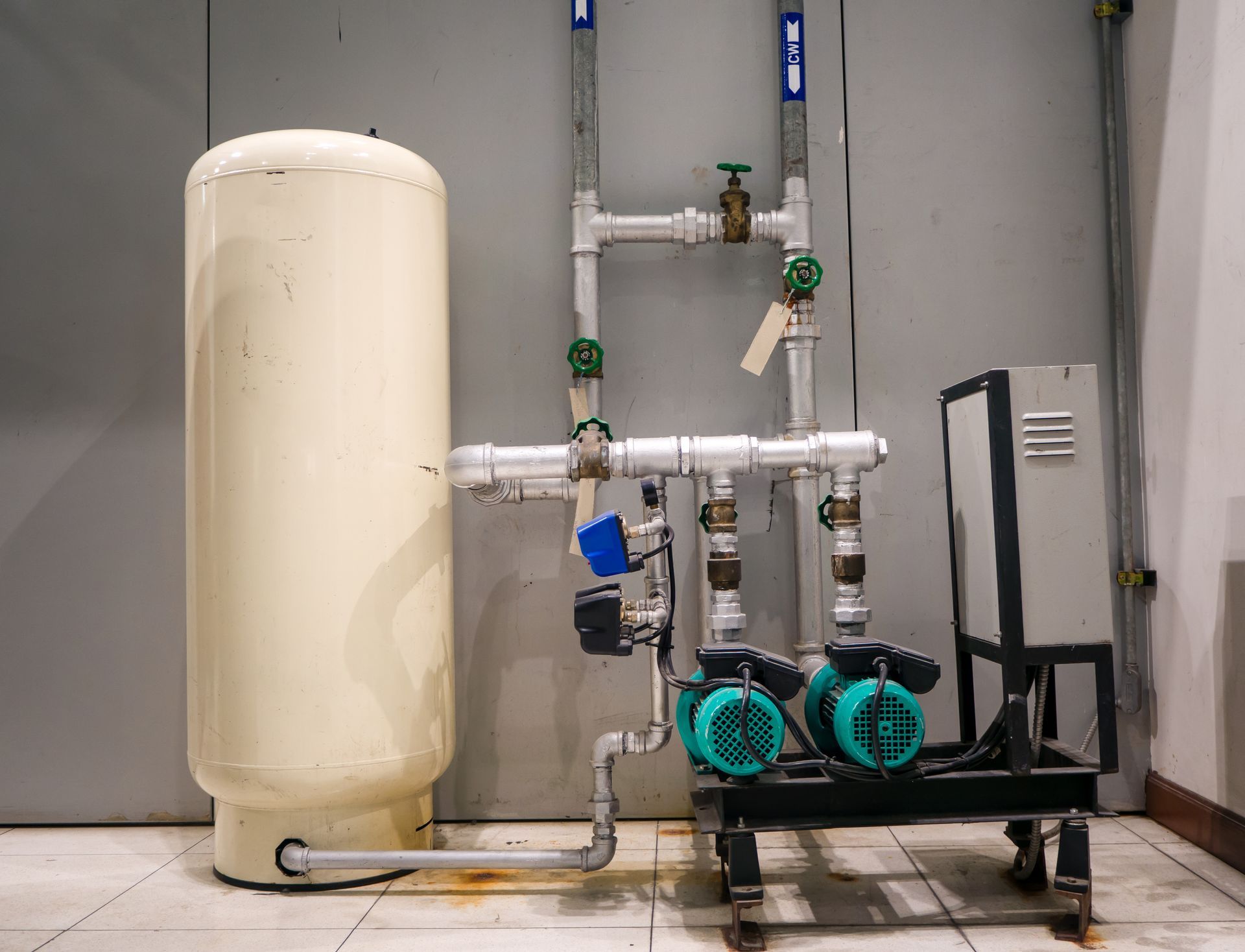 Water treatment setup with beige tank, pipes, and two green pumps in a utility room