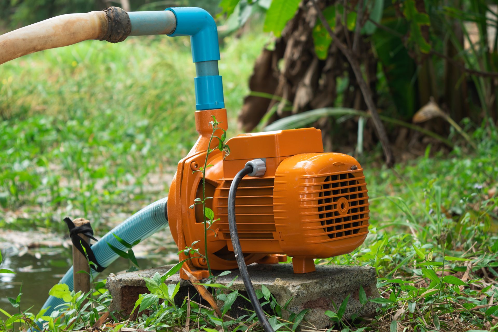 Orange water pump with blue pipe hose spraying water on grass outdoors