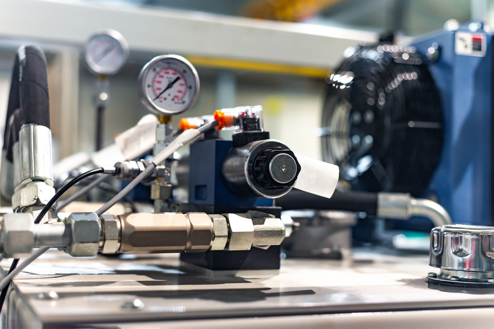Close-up of industrial machinery with pressure gauge, metal fittings, and blue equipment on a workbench