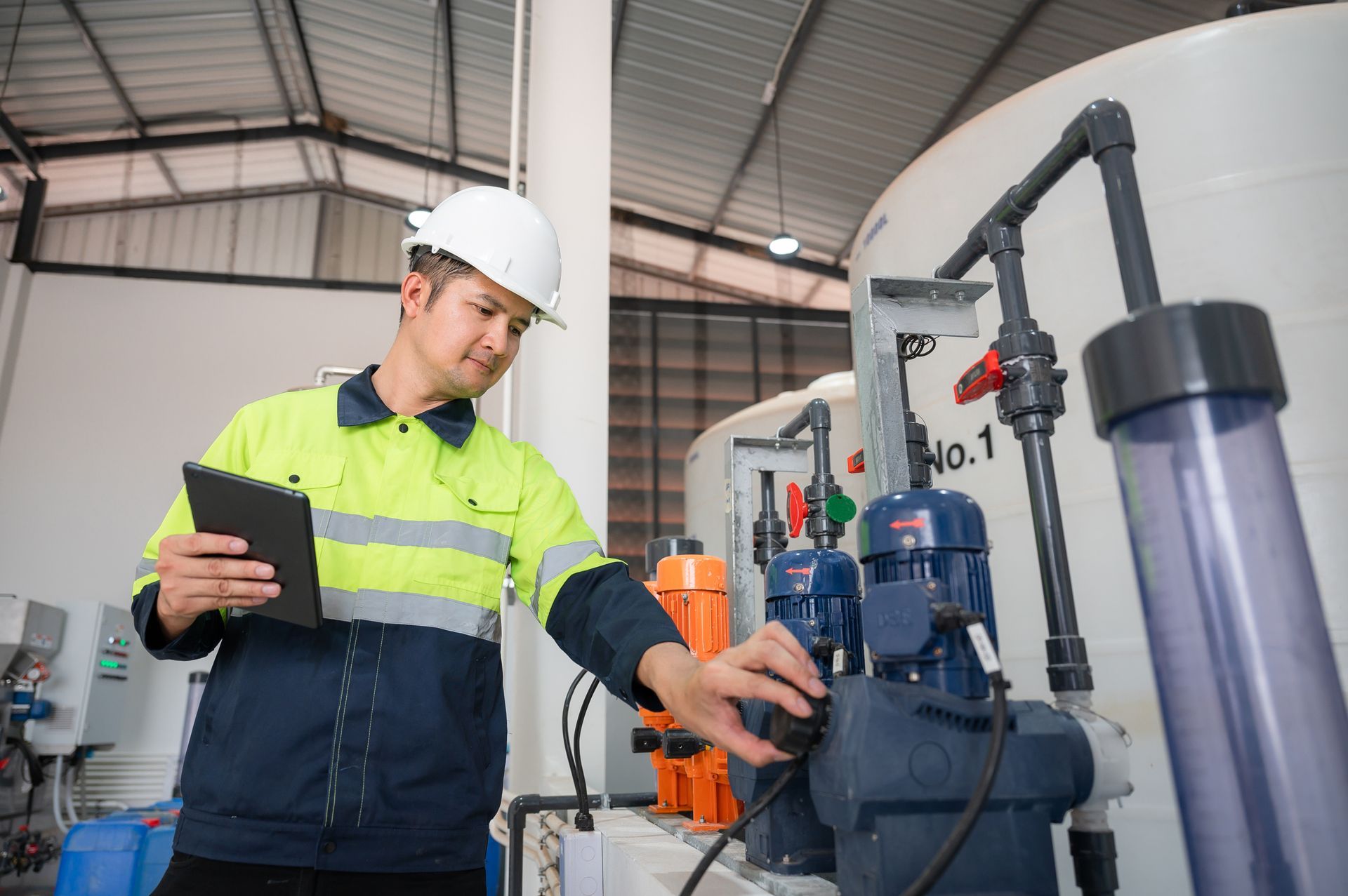 A man wearing a safety vest inspects valves inside a large industrial facility.