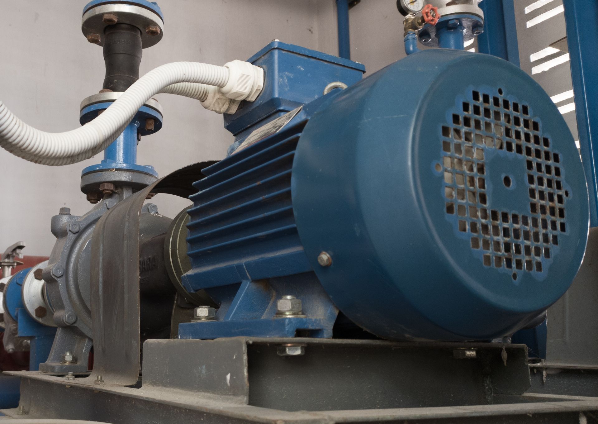 Blue industrial pump motor in a mechanical room, with pipes and wiring attached
