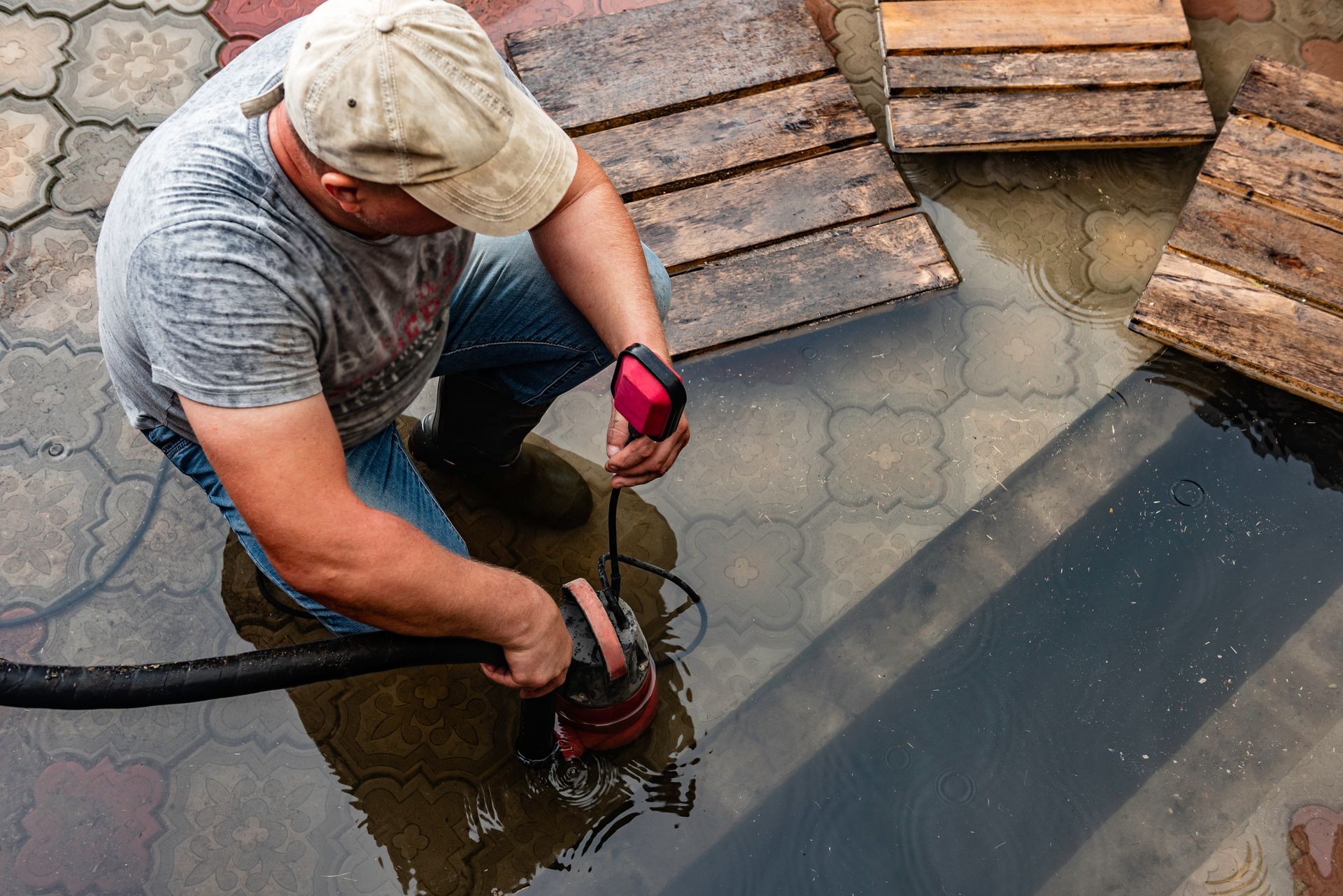 Worker using a drill to cut through wet concrete beside stacked pavers and a black tarp.