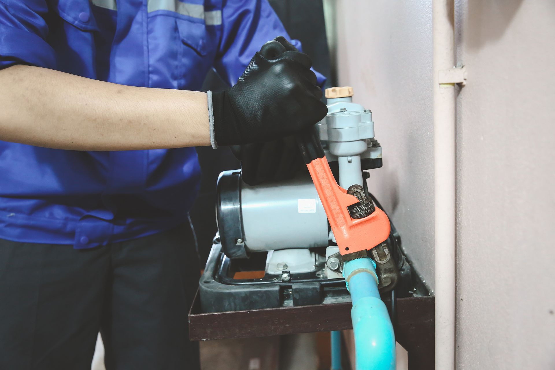 A man wearing a blue shirt and black gloves repairs a water pump, focused on his task.