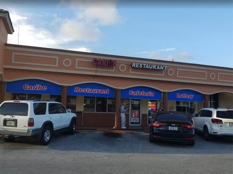 Caribe Restaurant, exterior view, featuring a tan building with blue awnings and parked cars.