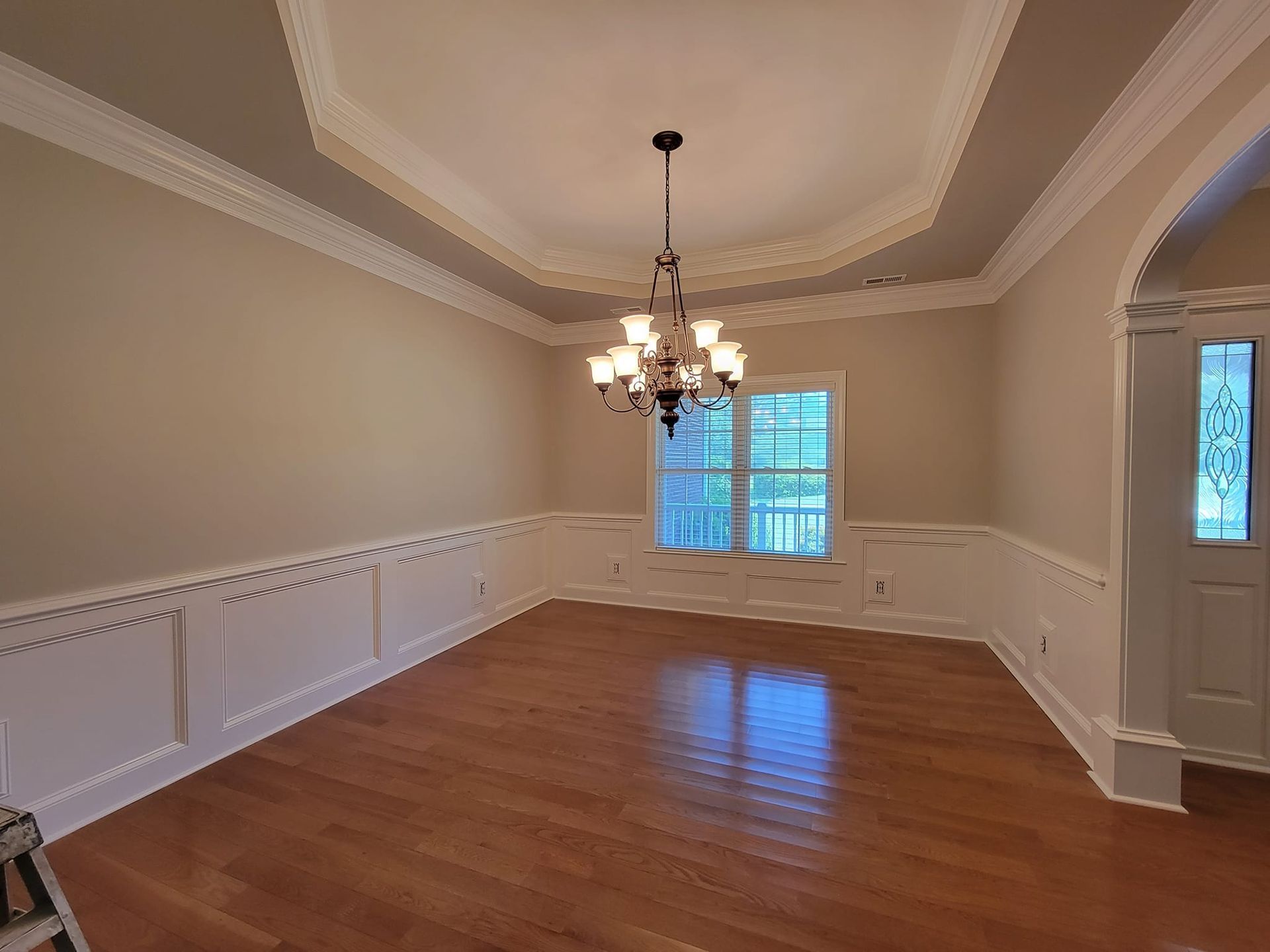 An empty dining room with a chandelier hanging from the ceiling.