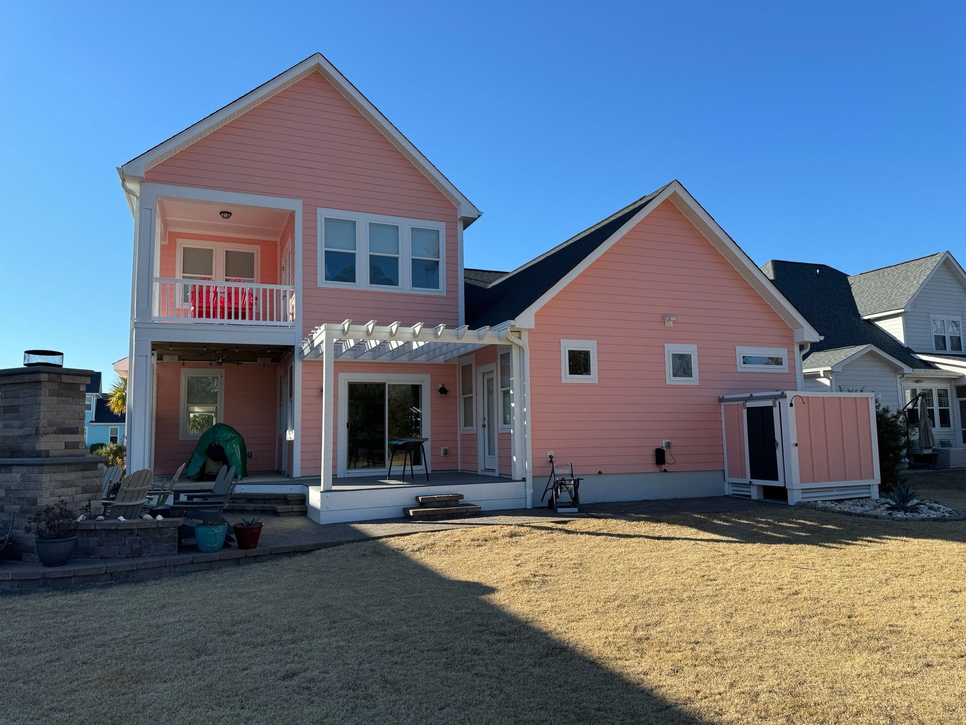 A pink house with white trim and a pergola in the backyard