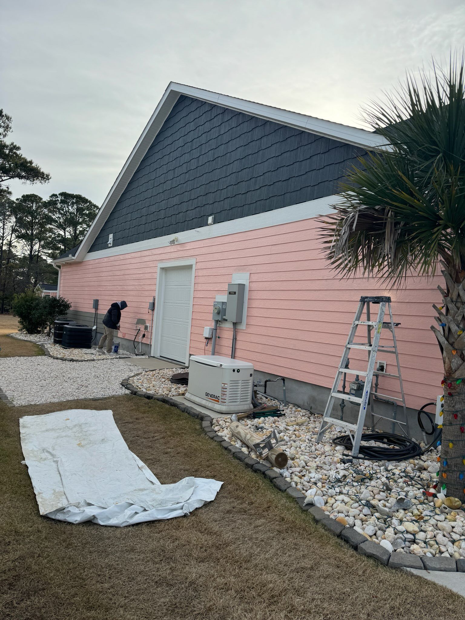 A pink house is being painted in a yard with a ladder.