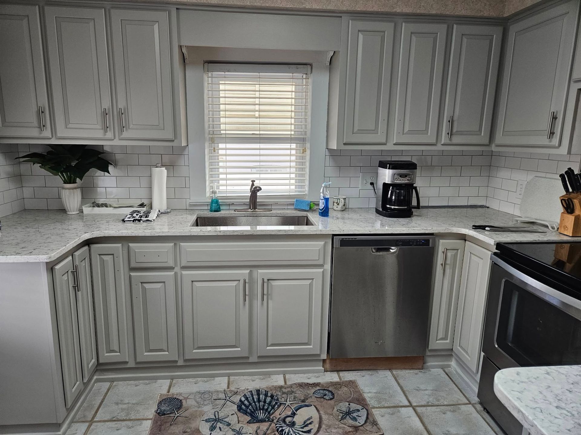 A kitchen with white cabinets , stainless steel appliances , a sink and a window.