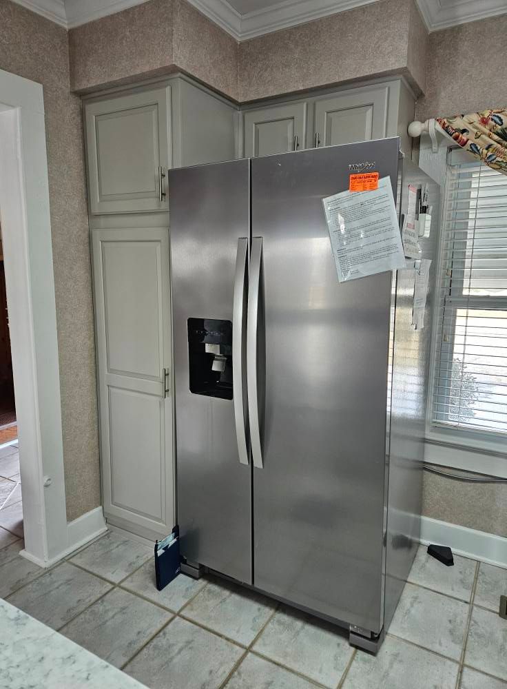 A stainless steel refrigerator is sitting in a kitchen next to a window.