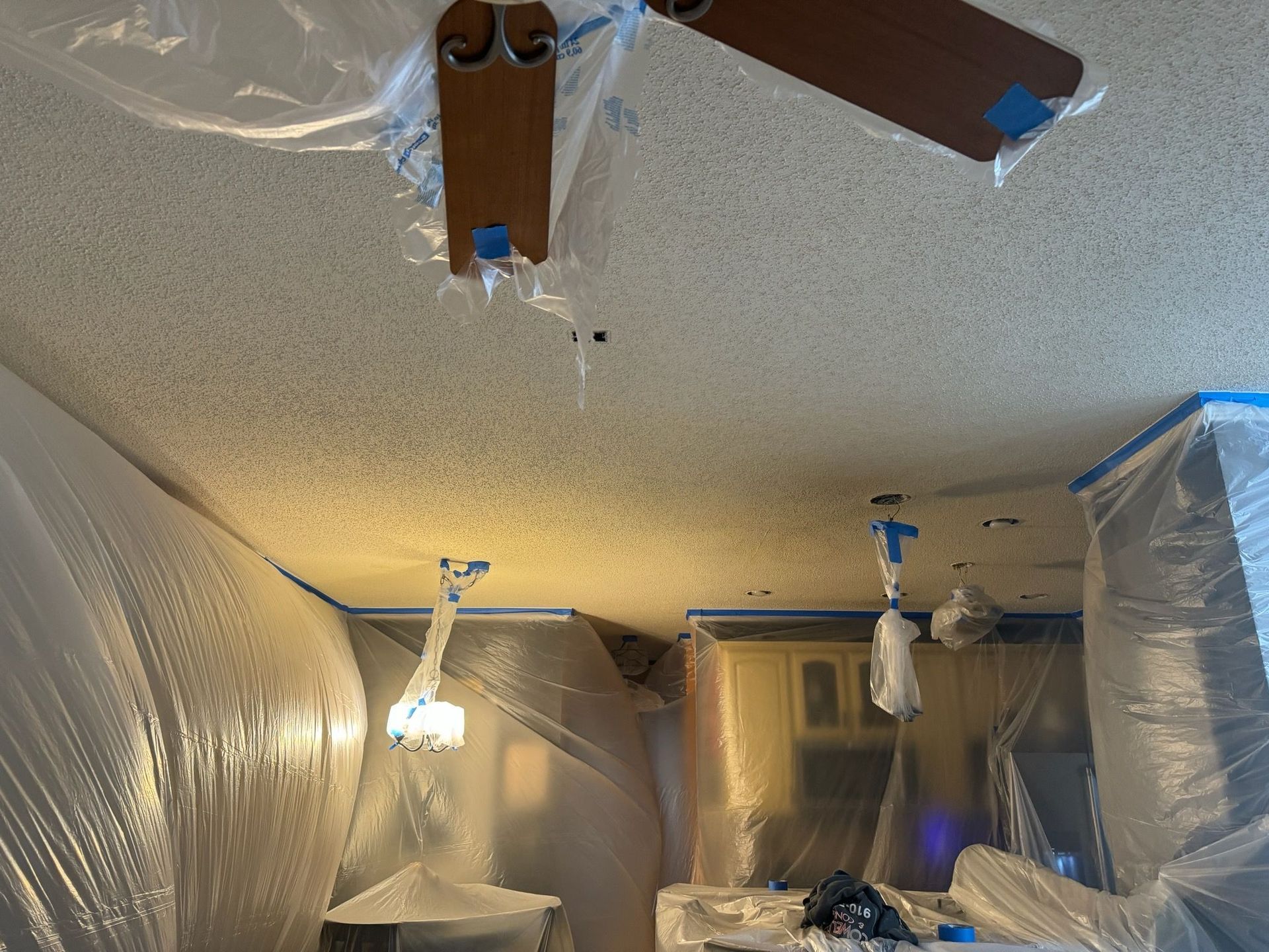 A ceiling fan is hanging from the ceiling of a room covered in plastic.