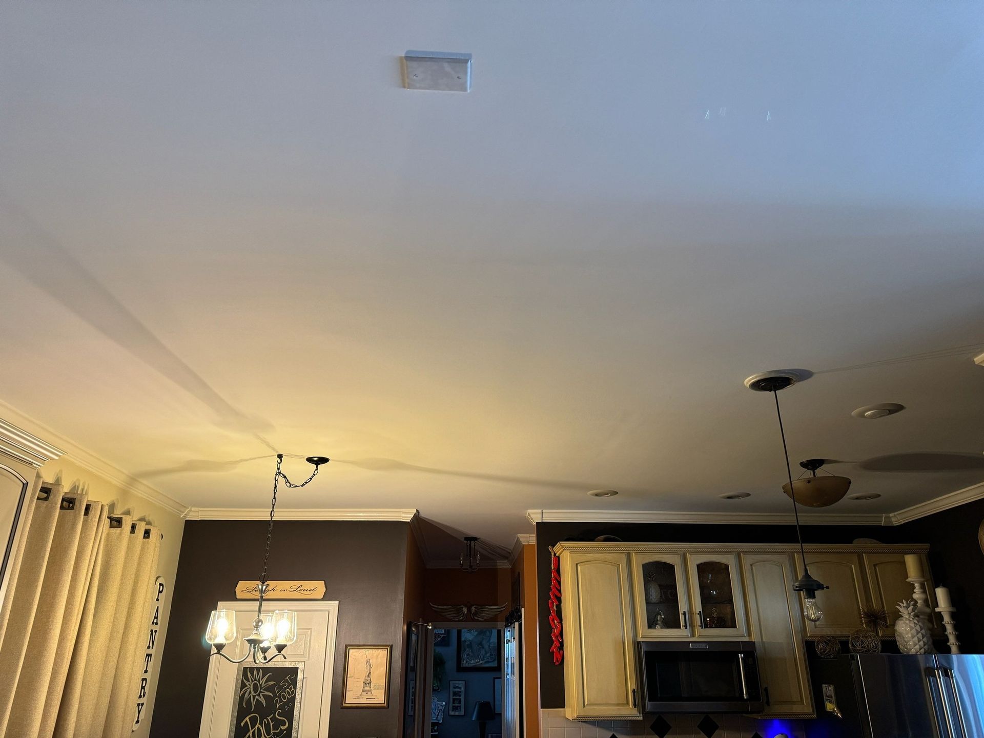 A kitchen with a white ceiling and a chandelier hanging from it.