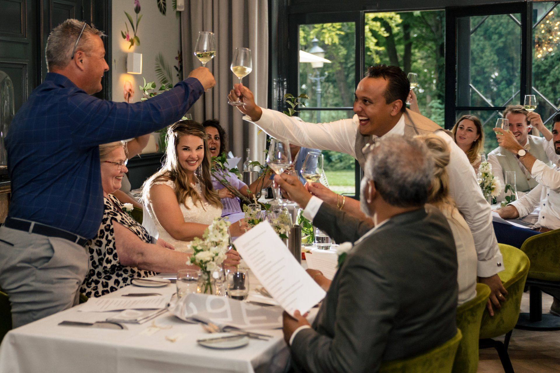 Een groep mensen zit aan een tafel in een restaurant en brengt een toost uit met wijnglazen.