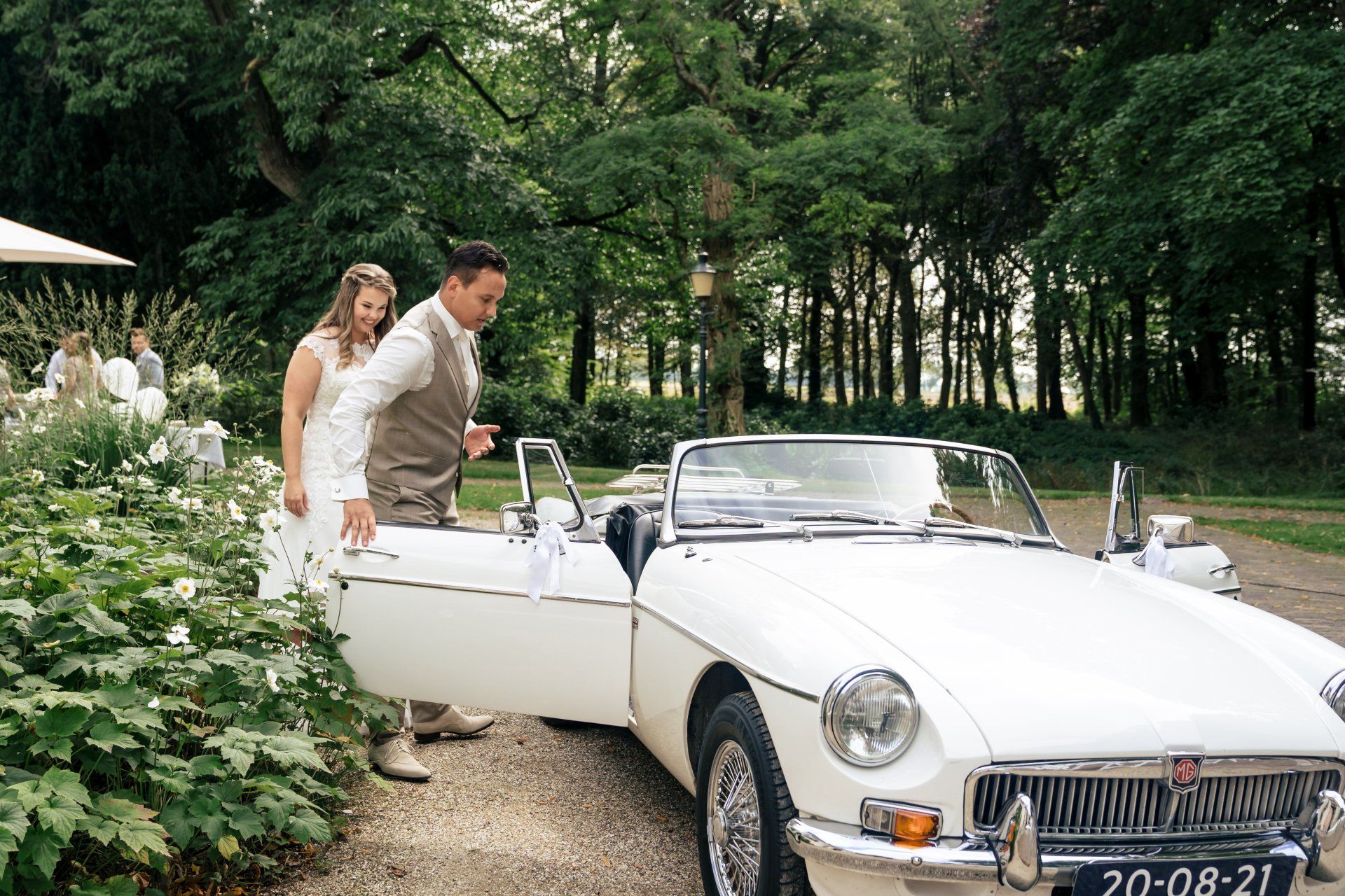 Een bruid en bruidegom staan ​​naast een witte cabriolet.