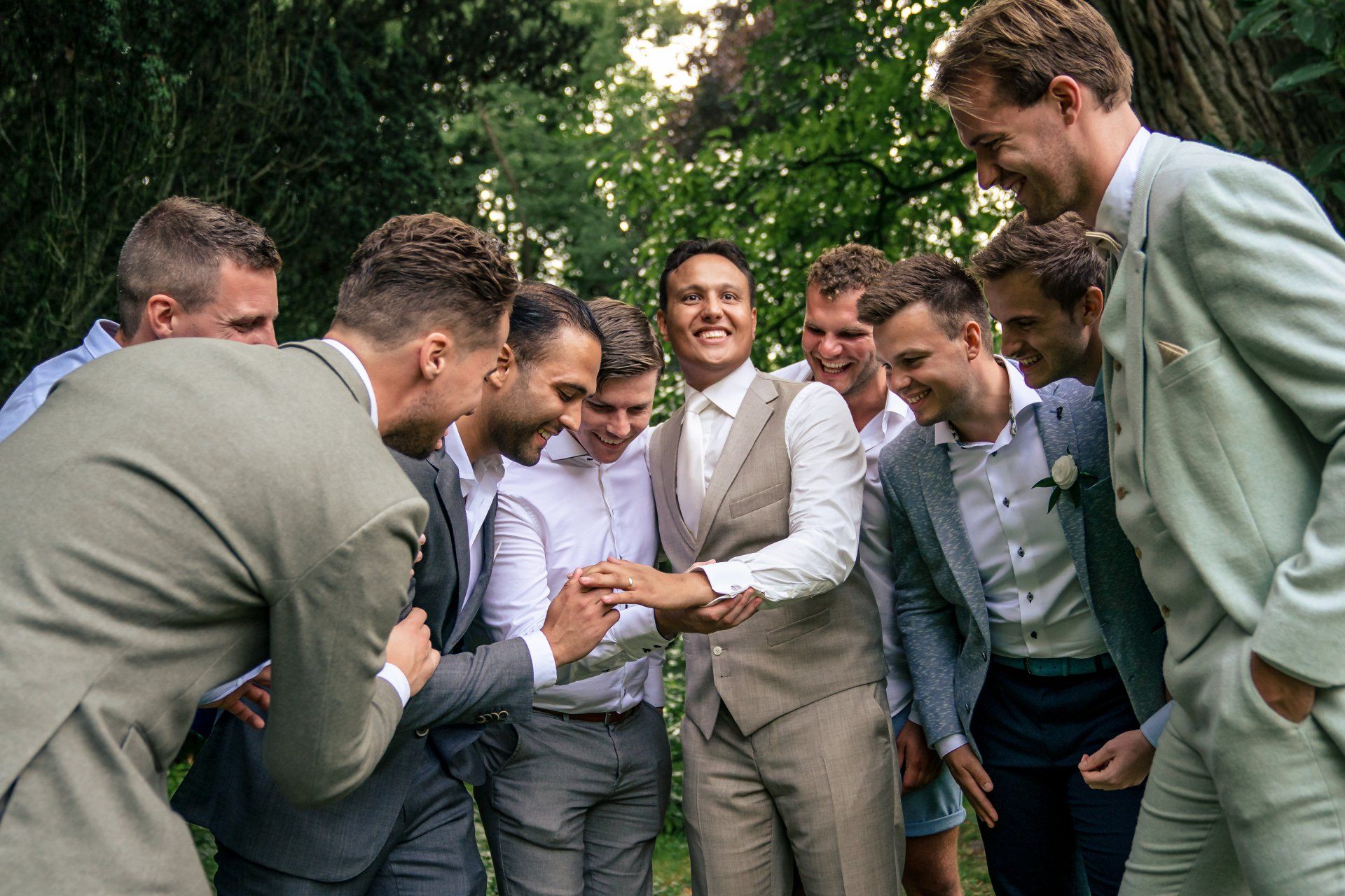 Een groep mannen in pak staat rond een bruid en bruidegom.