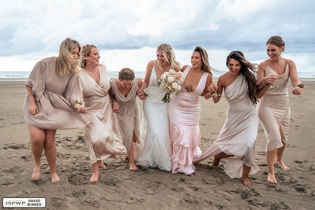 Een bruid en haar bruidsmeisjes poseren voor een foto op het strand.
