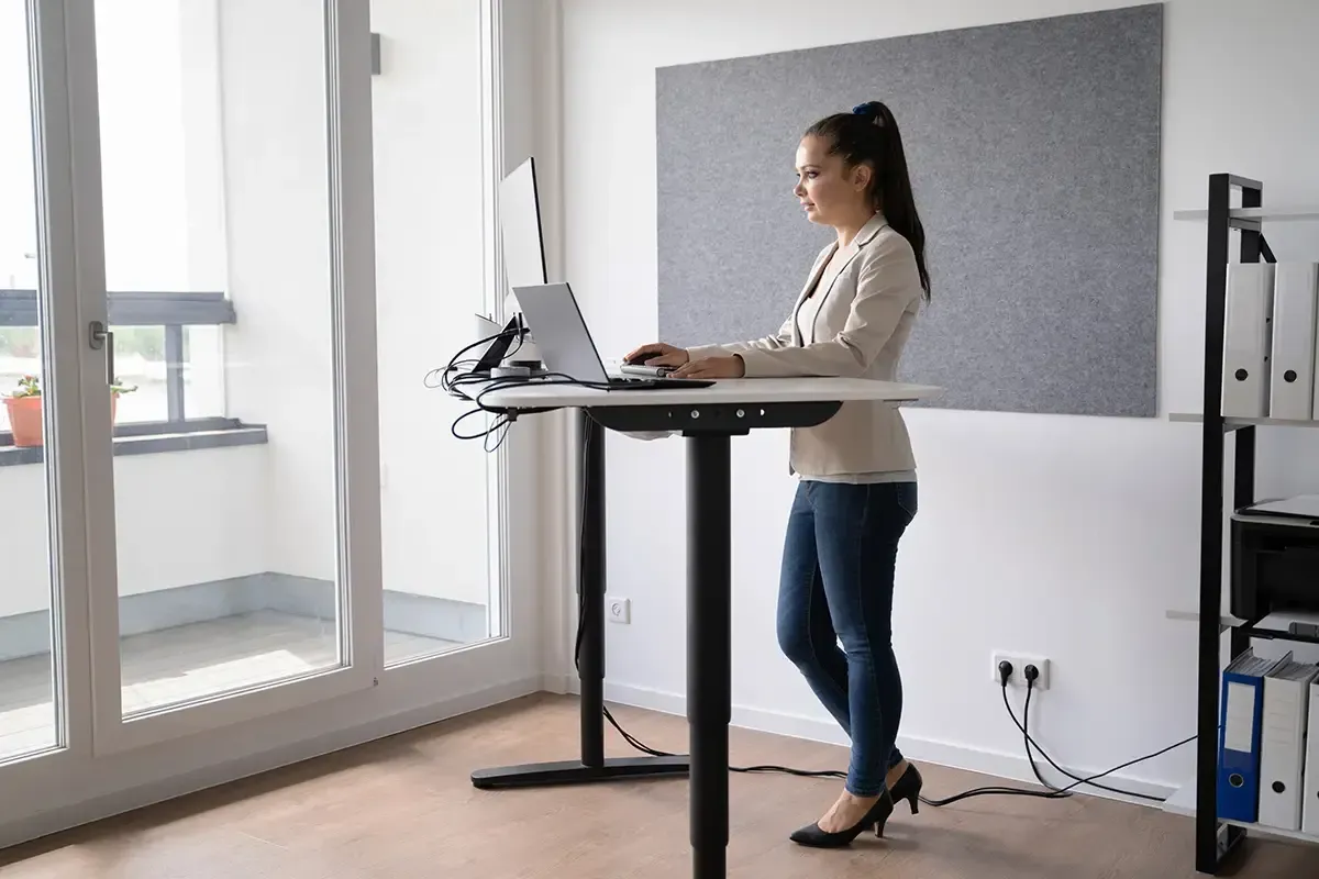 Een vrouw staat achter een staand bureau en gebruikt een laptop.