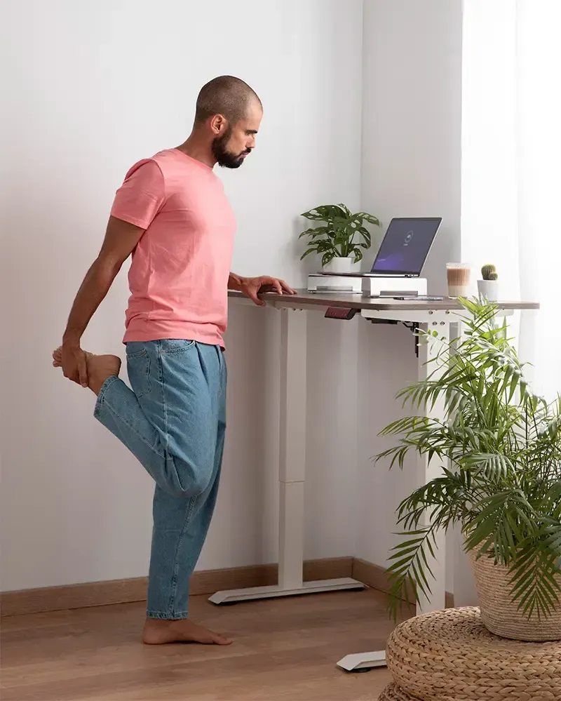 Een man strekt zijn been terwijl hij aan een staand bureau staat.