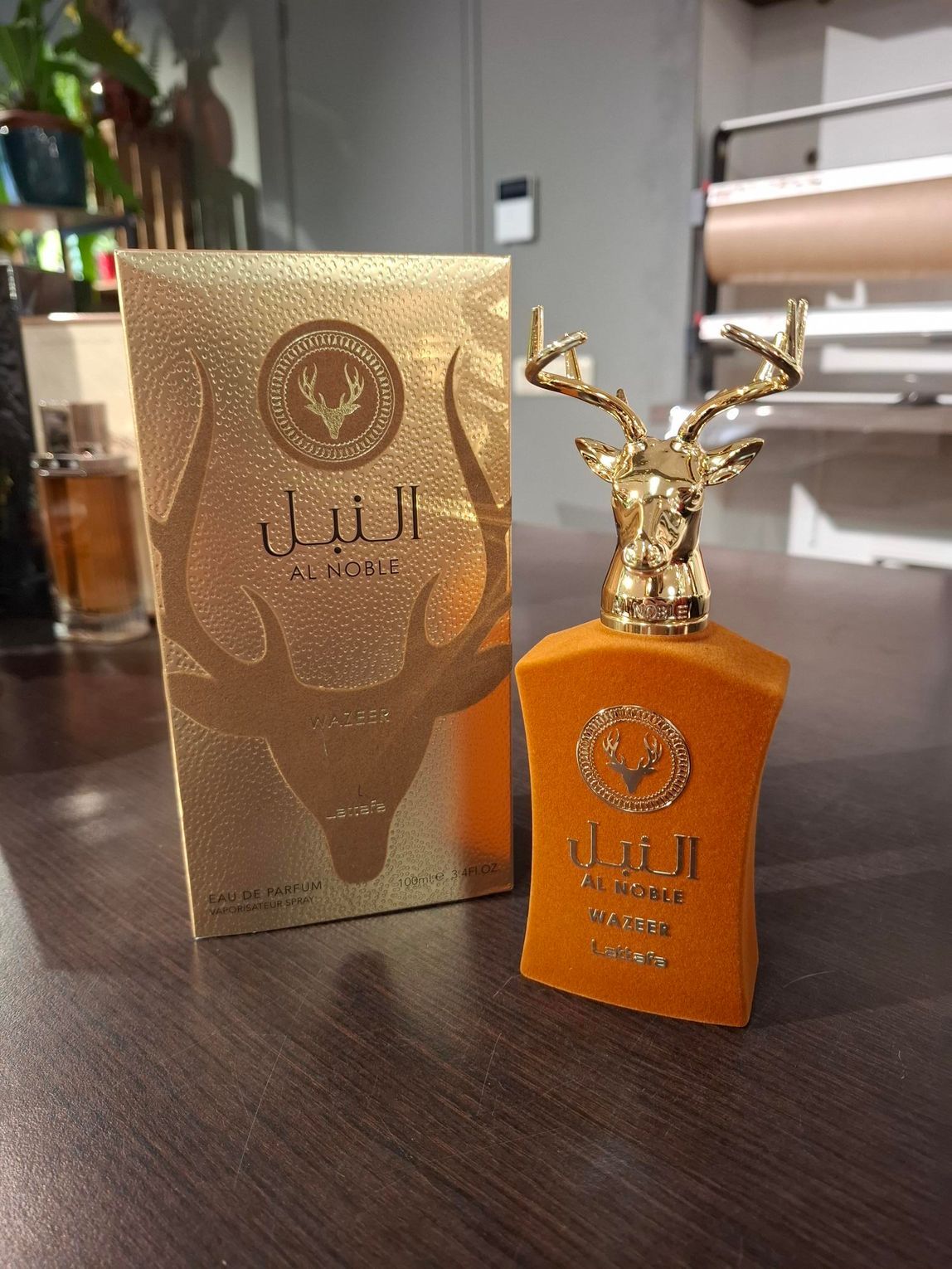 Een goudkleurige parfumdoos en een bijpassende oranje fluwelen fles met een gouden hertenkopdop op een houten tafel.