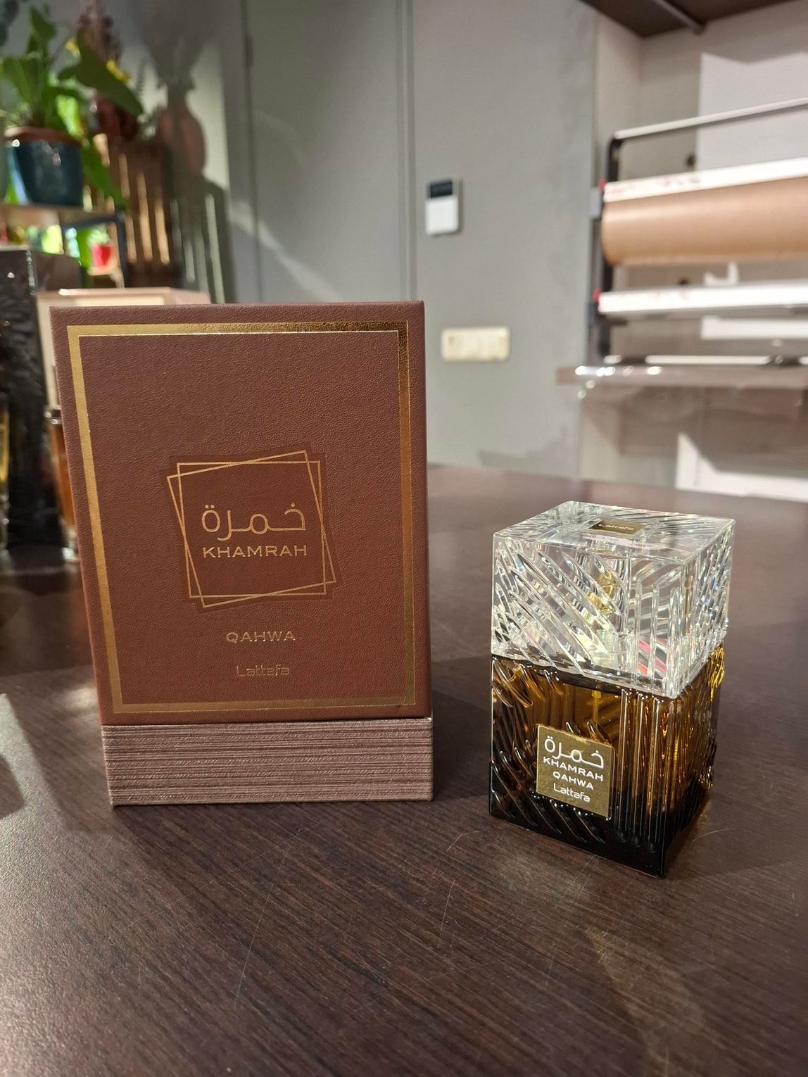 Het parfumflesje Lattafa Khamrah staat naast de bruine, gestructureerde doos, tentoongesteld op een houten ondergrond.