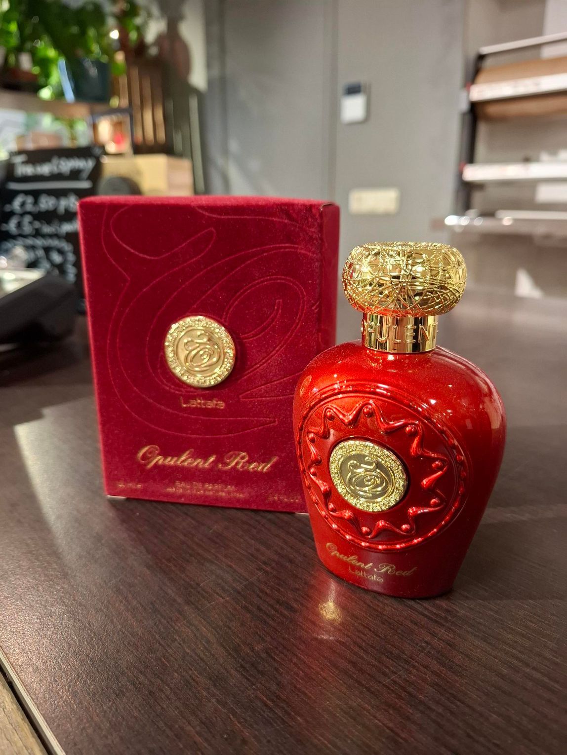 Een rode parfumfles en de bijbehorende rode fluwelen doos met gouden ronde emblemen staan op een donkere houten tafel.