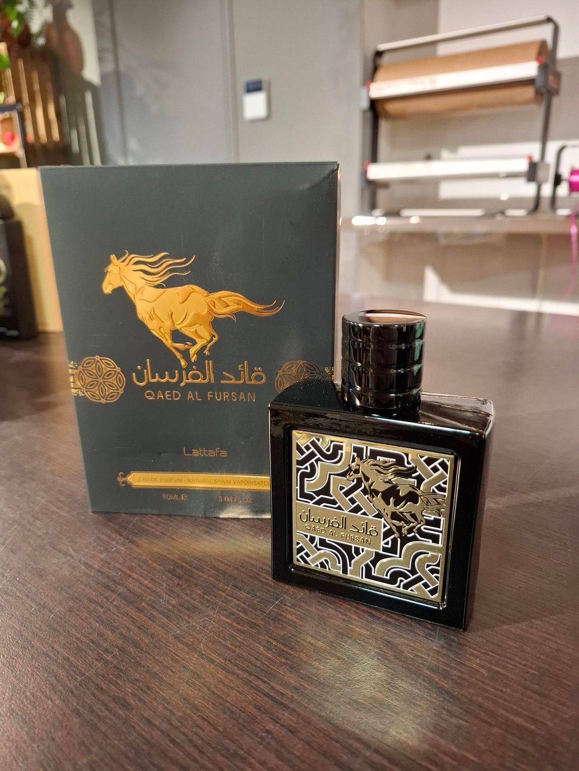 Een flesje Qaed Al Fursan-parfum in een donkere doos met een gouden paardenlogo op een houten oppervlak.