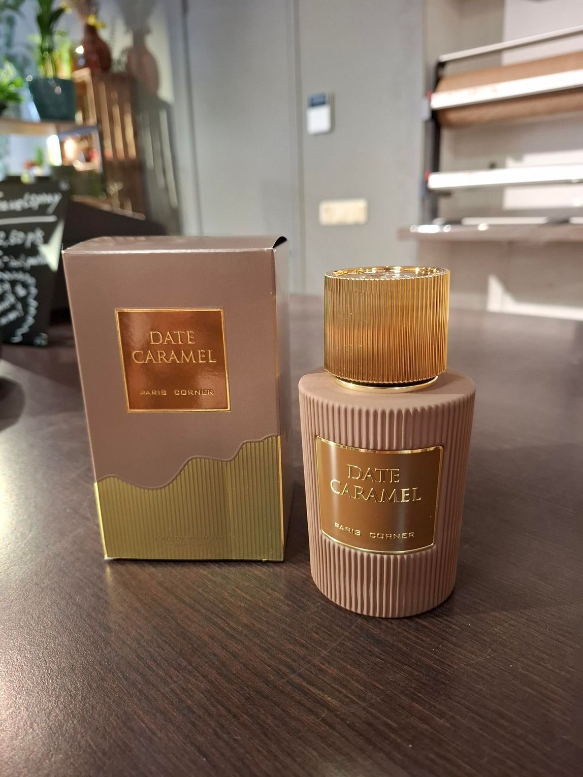 Een beige en gouden parfumflesje Oud Caramel, naast het bijbehorende doosje, staat uitgestald op een houten ondergrond.
