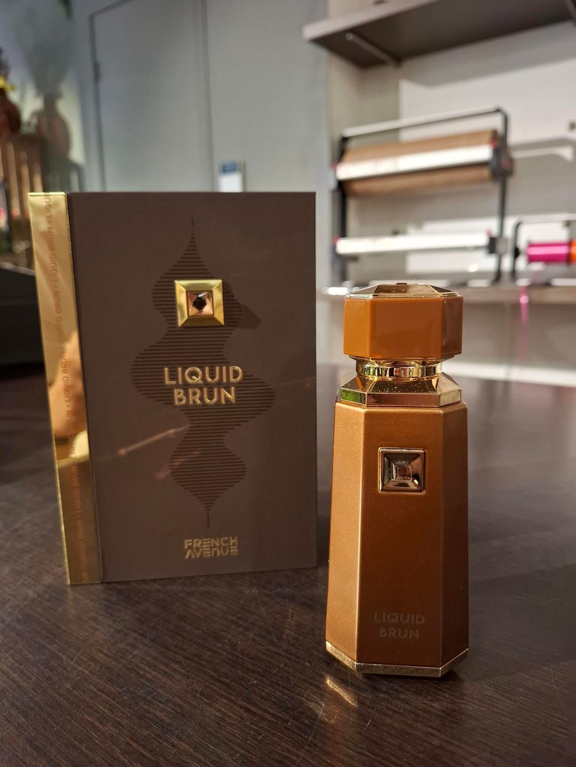 Een bronskleurig parfumflesje staat naast de bijbehorende bruine doos met het opschrift