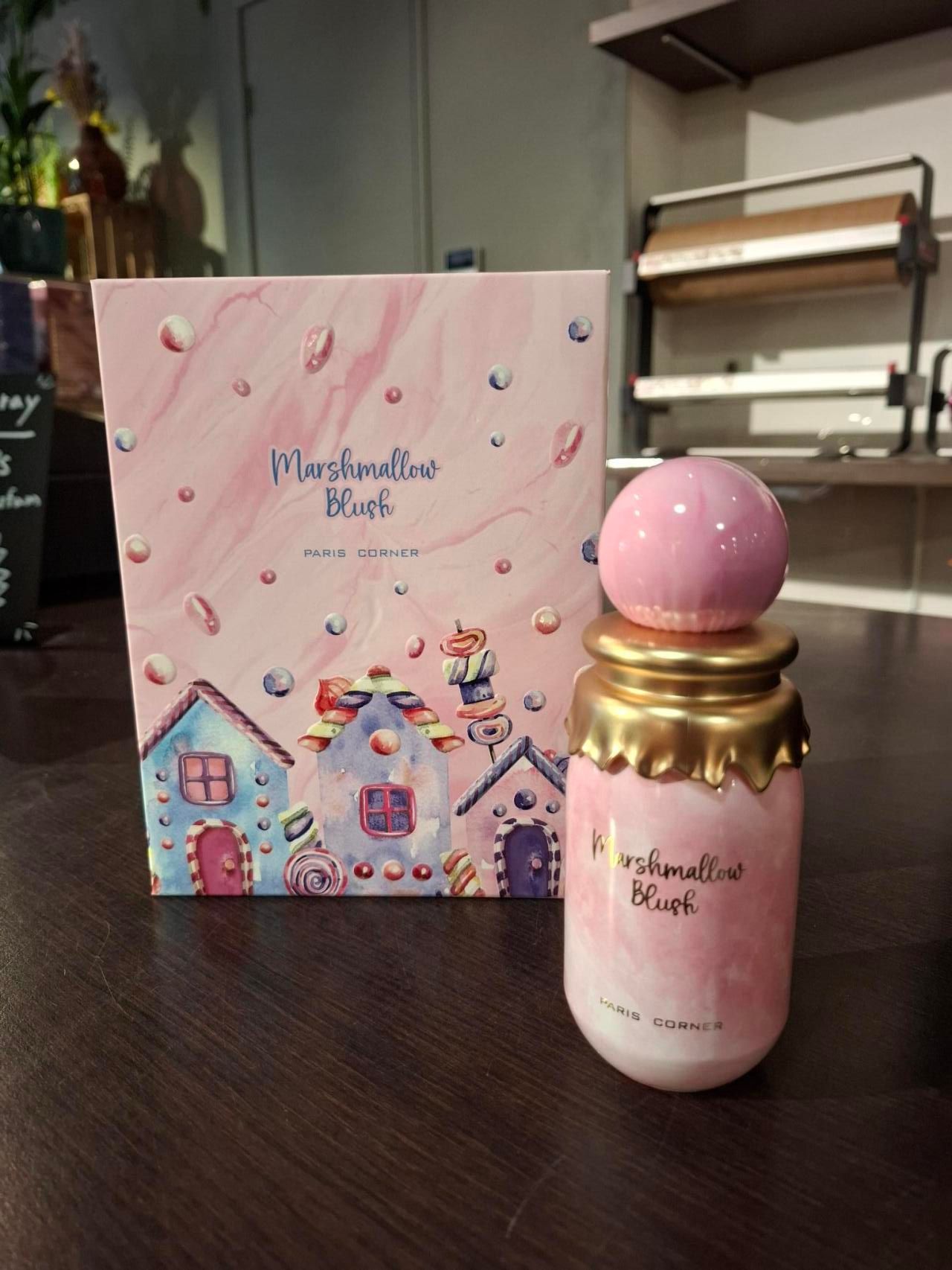 Een flesje Marshmallow Bliss-parfum staat op een donkere ondergrond naast de bijpassende roze geschenkdoos met afbeeldingen.