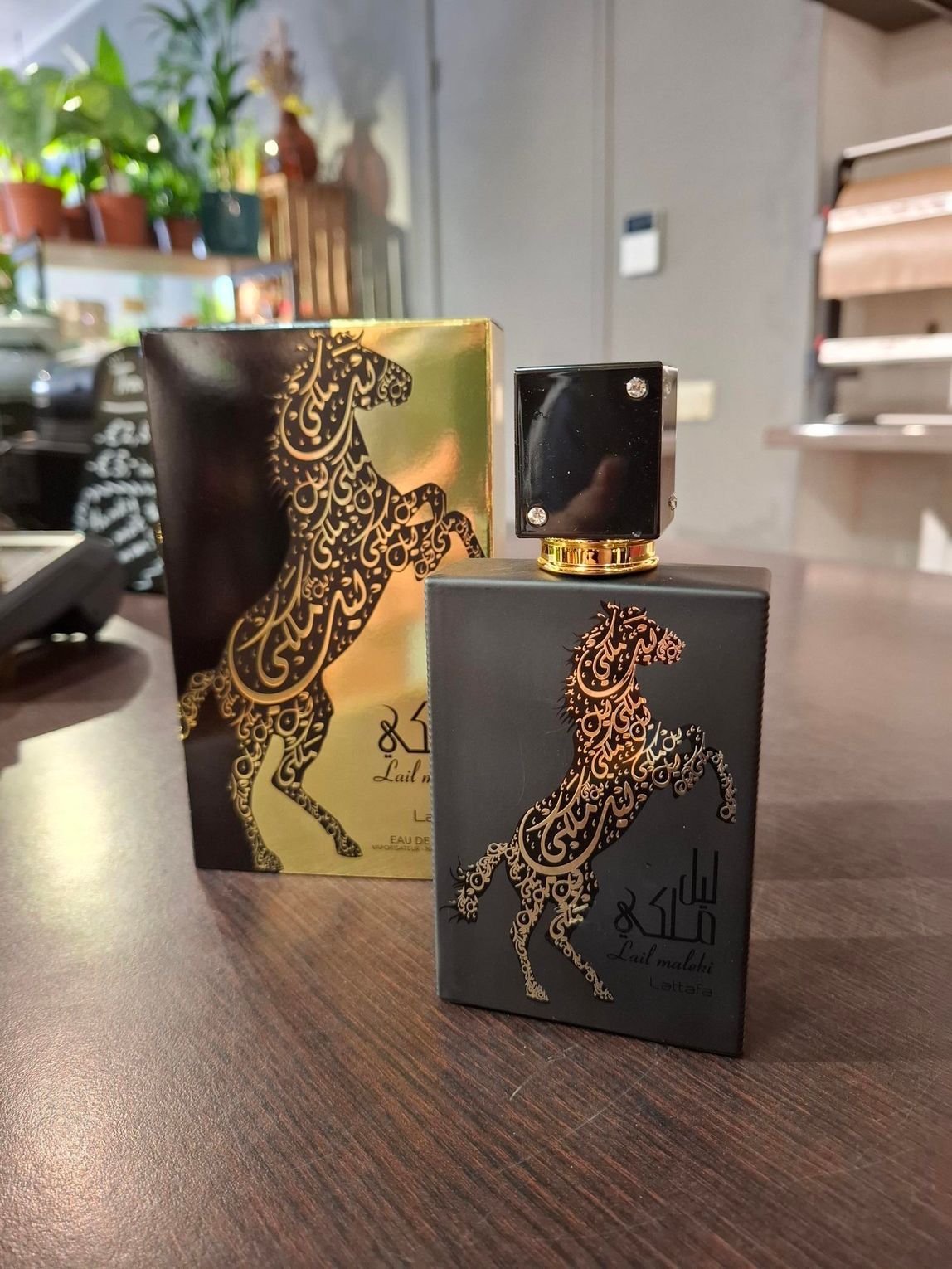Een zwarte parfumfles en de bijbehorende gouden doos, beide met een decoratieve gouden paardensilhouet, staan op een houten ondergrond.