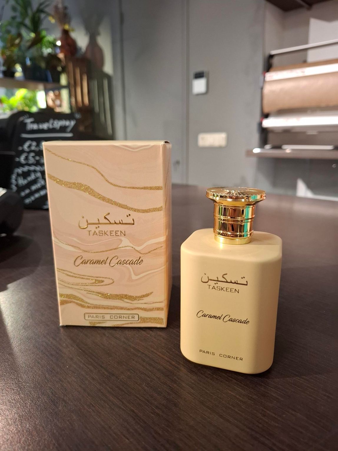 Een flesje Taskeen Caramel Cascade parfum en het bijbehorende beige doosje staan op een houten oppervlak.