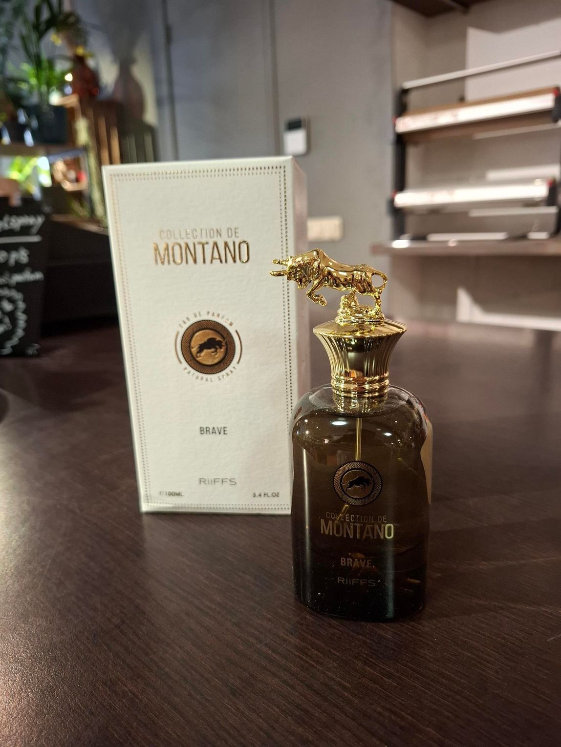 Een flesje Montano-parfum met een gouden stierdop, staand naast de witte doos op een donkere ondergrond.