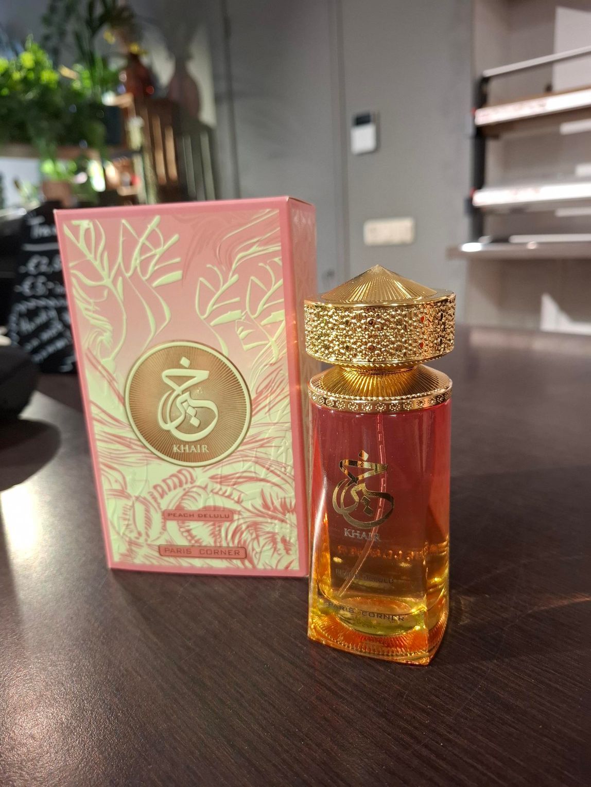 Op een houten tafel staan een roze doos en een bijpassend glazen parfumflesje met een goudkleurige dop.