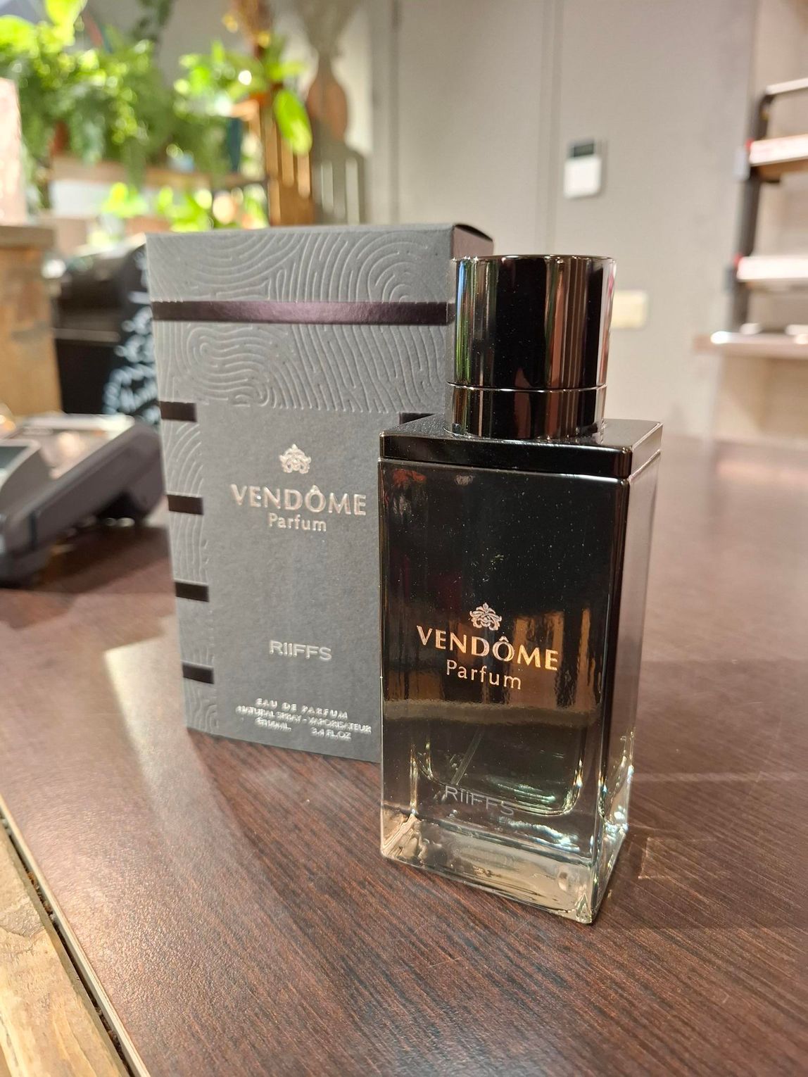 Een fles Vendôme Parfum met de bijbehorende grijze doos, staand op een houten ondergrond.