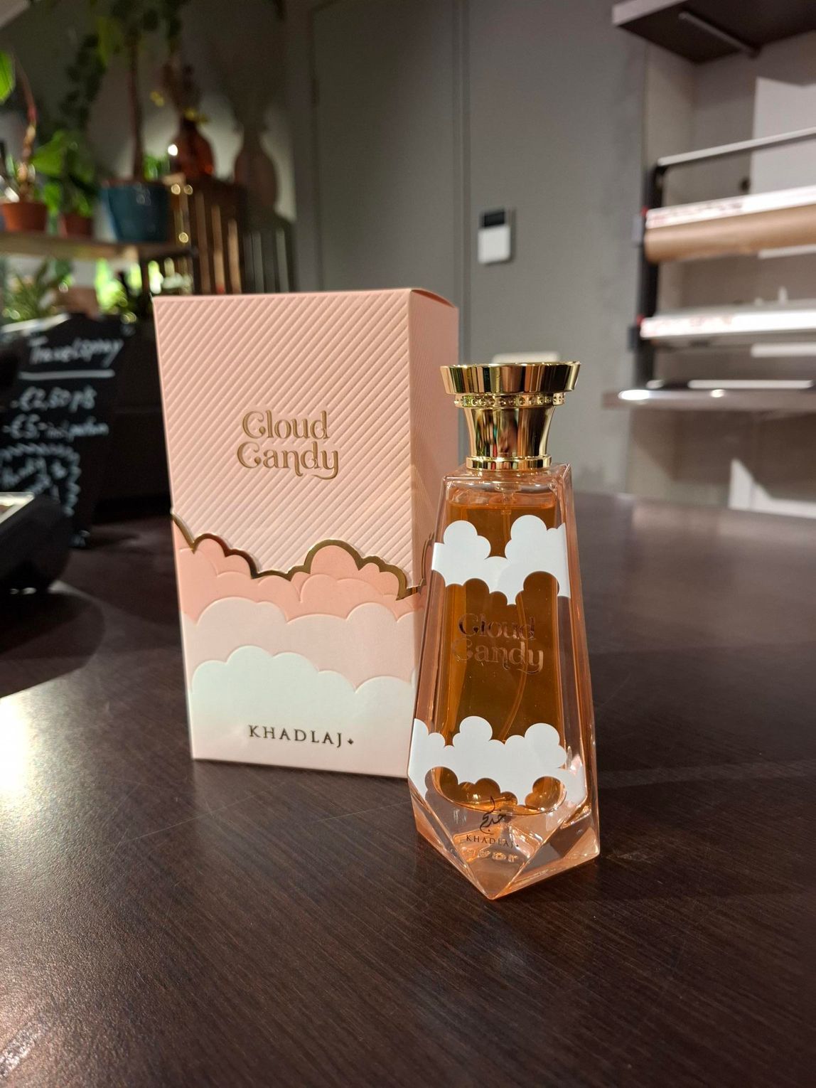 Een perzikkleurig flesje Cloud Candy-parfum en het bijbehorende doosje met een wit wolkje staan op een donkerhouten ondergrond.